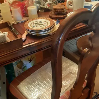 Dining table setup featuring a high-back wooden chair, stacked patterned ceramic plates, pillar candles, and various household wares.