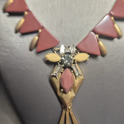 Sale Photo Thumbnail #264: A J. Crew statement necklace featuring a brass-tone chain and hardware. The design showcases geometric triangular elements in a deep burgundy/maroon hue, accented with clear rhinestones, a central marquise-cut stone, and dangling brass-tone spikes. Includ