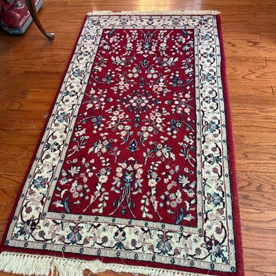 Small Persian-style area rug featuring a crimson field with intricate floral motifs, cream floral border, and fringed ends.