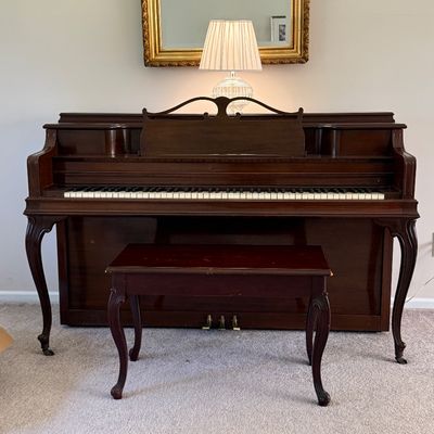 Vintage dark mahogany upright Janssen piano featuring cabriole legs and an ornate music stand, complete with a matching wooden bench.