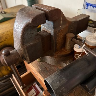 Vintage heavy-duty Columbian cast iron bench vise mounted on a wooden workbench, showing surface rust and age-appropriate wear.