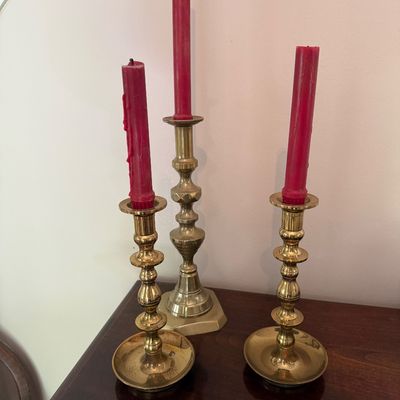 Set of three vintage brass candlesticks of varying heights, holding red taper candles with visible wax drip.