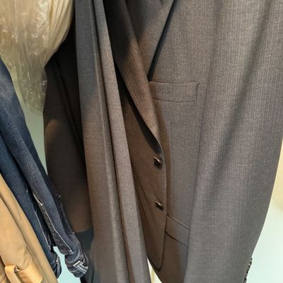 Dark gray charcoal pinstripe two-piece men's suit jacket and matching trousers hanging in a closet.