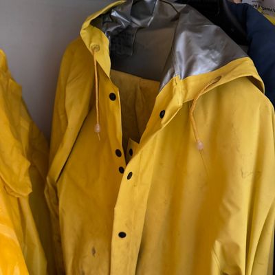 Vintage heavy-duty yellow raincoat featuring a metallic silver-lined hood, drawstring toggles, and black snap buttons, hanging on a wire...