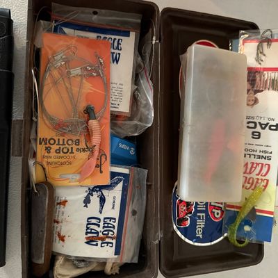 Open plastic tackle box filled with vintage fishing supplies, including Eagle Claw hooks, wire leaders, and soft plastic lures, alongside...