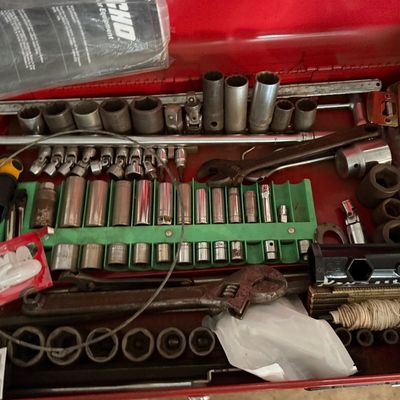 Red metal toolbox filled with an assortment of socket sets, ratchets, extensions, adjustable wrenches, and hardware accessories.