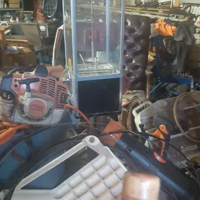 Vintage glass and metal claw arcade machine alongside various workshop tools, including a Stihl leaf blower.