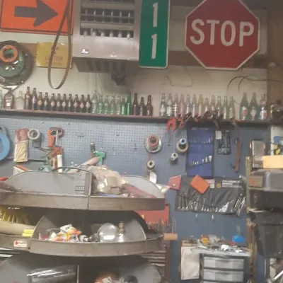 Workshop loaded with vintage road signs, a metal revolving bin organizer, glass bottles, tools, and hardware.