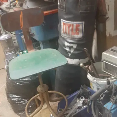 Vintage metal swivel shop stool with green seat alongside a black Title Boxing heavy bag and workshop tools.