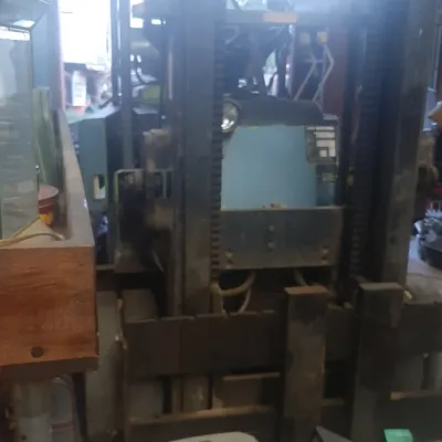 Vintage blue industrial forklift with a tall mast, stored indoors alongside various tools and hardware.