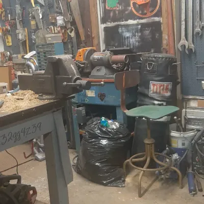 Workshop loaded with various hand tools, bench vise, grinding wheel, industrial stool, and Title punching bag.