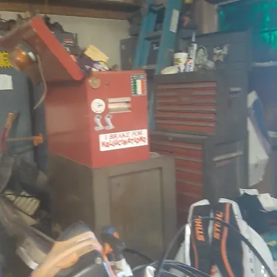 Garage workshop filled with tools, including a red metal toolbox with stickers, a Stihl weed trimmer, extension cords, and a blue...