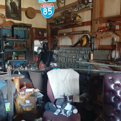 Workshop and garage area filled with various goods including office chairs, power tools, road signs, novelty decor, and shelving units.