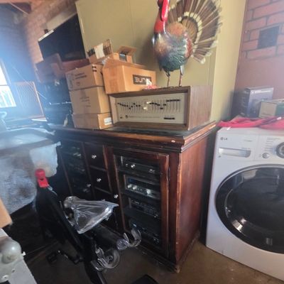 Sale Photo Thumbnail #7: Vintage dark wood media console filled with audio components, topped with a vintage graphic equalizer, turkey statue, and cardboard boxes, beside a modern white LG washing machine.