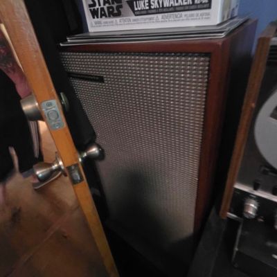 Sale Photo Thumbnail #11: Vintage stereo speaker cabinet with a wood veneer frame and textured metallic grille cloth, positioned next to audio equipment.