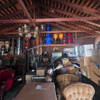 Sale Photo Thumbnail #16: Large garage workshop filled with vintage drum sets, various musical equipment, armchairs, and stacked storage boxes.