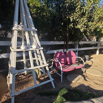 Sale Photo Thumbnail #32: Tall white wooden garden obelisk trellis alongside a vintage pink metal shell-back patio bench in a yard setting.
