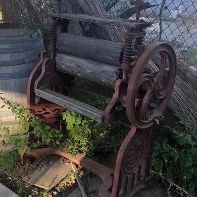 Sale Photo Thumbnail #33: Antique cast iron and wooden laundry wringer mangle machine, featuring heavy rusted iron framing, large hand crank wheel, and top tension screws.