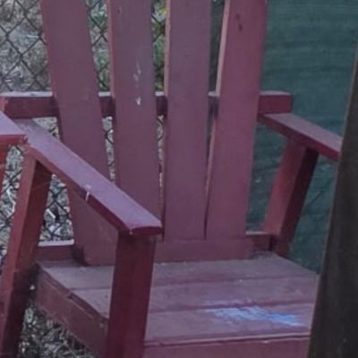Sale Photo Thumbnail #35: Red painted wooden Adirondack-style lawn chair featuring a slatted back and wide armrests, showing minor surface wear and weathering.