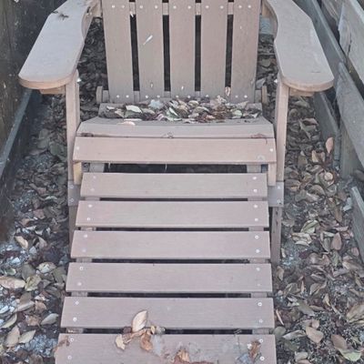 Sale Photo Thumbnail #43: Brown composite wood Adirondack chair with an attached pull-out footrest, placed outdoors in a yard area.