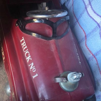 Sale Photo Thumbnail #48: Vintage red fire department pedal car featuring "TRUCK No. 1" lettering, a metal steering wheel, windshield frame, and a hood ornament.