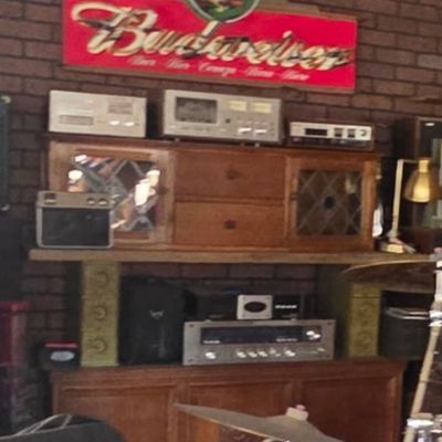 Sale Photo Thumbnail #55: Vintage stereo audio components displayed on wooden cabinets below a Budweiser bar sign, with a drum set visible in the foreground.