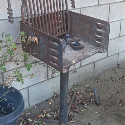Sale Photo Thumbnail #58: Heavy-duty outdoor park-style charcoal grill on a metal pedestal base, showing significant surface rust and wear.