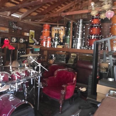 Sale Photo Thumbnail #60: A workshop space packed with various drum sets, congas, audio equipment, and red velvet Victorian-style armchairs.