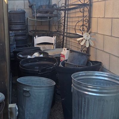 Sale Photo Thumbnail #62: Outdoor patio corner containing galvanized trash cans, plastic planters, a wrought iron baker's rack, and various garden items.