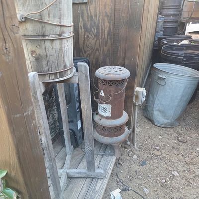 Sale Photo Thumbnail #66: Vintage rusted cast iron kerosene parlor heater alongside a rustic wooden bucket and metal trash cans.