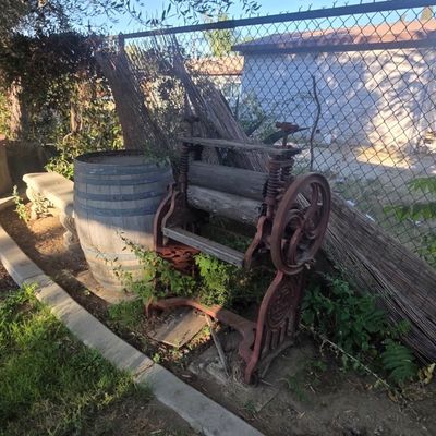 Sale Photo Thumbnail #71: Antique cast iron clothes wringer and a weathered wooden barrel in a yard setting.
