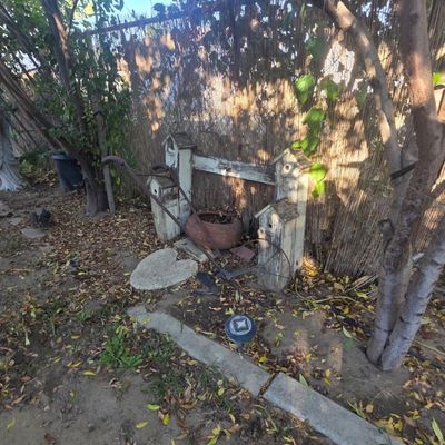Sale Photo Thumbnail #75: Rustic garden decor setup including painted wooden birdhouses, an antique manual walk-behind plow, and a terra cotta planter placed along a bamboo fence line.