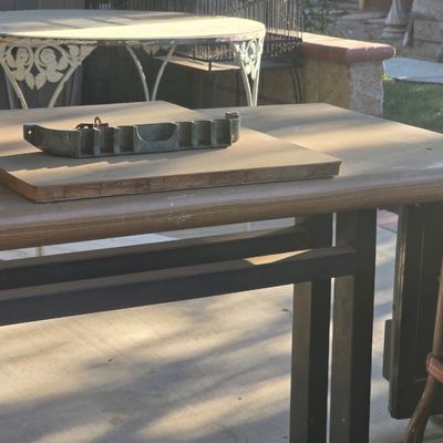 Sale Photo Thumbnail #76: Outdoor workbench with a metal casting mounted on a thick butcher-block wood board, accompanied by additional patio furniture in the background.