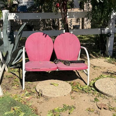Sale Photo Thumbnail #89: Vintage pink metal two-seat lawn glider bench with white frame, displaying minor paint wear, set outdoors.