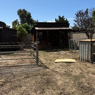 Sale Photo Thumbnail #102: Outdoor property featuring a metal livestock pen and several wooden outbuildings under a clear blue sky.