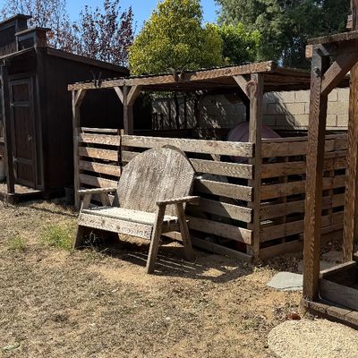 Sale Photo Thumbnail #103: Weathered rustic wooden garden bench positioned in front of a covered outdoor corral enclosure.