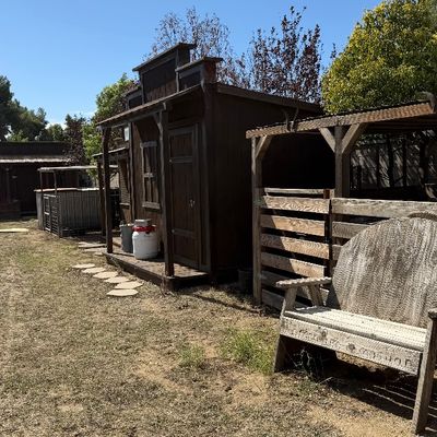 Sale Photo Thumbnail #104: Rustic Western-style outdoor playhouse or shed alongside a carved wooden bench in a yard.