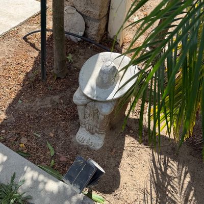 Sale Photo Thumbnail #106: Concrete garden statue depicting a sleeping figure wearing a sombrero, positioned outdoors alongside garden pathway stones and landscaping.