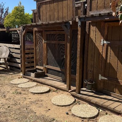Sale Photo Thumbnail #108: Rustic wooden Western-style outdoor shed and enclosed chicken coop structure with a wooden deck and round concrete stepping stones.