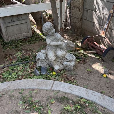 Sale Photo Thumbnail #113: Concrete garden statue depicting a seated child holding a small animal, accompanied by a vintage reel lawnmower and a bronze-tone street-clock style garden ornament.