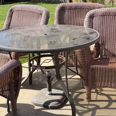 Sale Photo Thumbnail #124: Outdoor patio dining set featuring a round glass-top metal table with an umbrella base and four brown resin wicker armchairs.