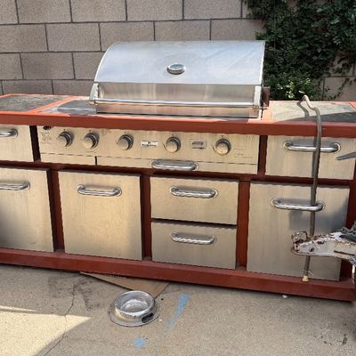 Sale Photo Thumbnail #125: Large custom stainless steel outdoor kitchen island with built-in gas grill, multiple drawers, and cabinet storage on a heavy-duty frame.