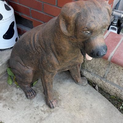 Sale Photo Thumbnail #128: Large cast stone or concrete dog statue depicting a seated boxer, featuring a weathered brown patina and expressive detailing.