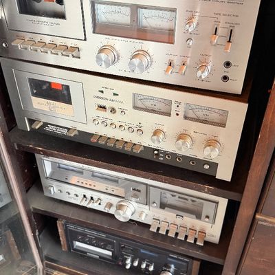 Sale Photo Thumbnail #150: Stack of vintage cassette tape decks housed in a wooden cabinet, including models from Kenwood, Akai, and JVC, circa late 1970s to early 1980s.
