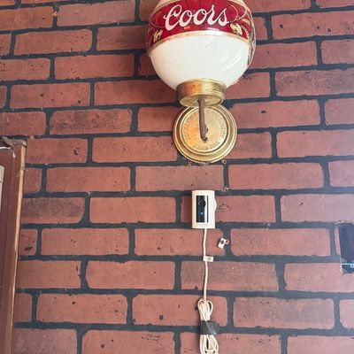 Sale Photo Thumbnail #155: Vintage Coors Beer globe sconce light mounted on a faux brick wall. The fixture features a round white globe with red brand lettering and a brass-tone base.