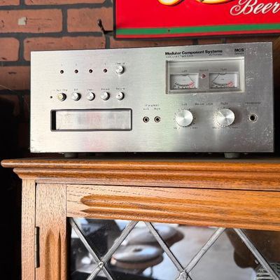 Sale Photo Thumbnail #176: Vintage Modular Component Systems (MCS) 3550 8-track tape deck by JCPenney, featuring dual VU meters and brushed aluminum faceplate, resting next to a Fender Rumble 15 bass amplifier.