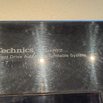 Sale Photo Thumbnail #189: Detail view of a vintage Technics Quartz SL-7 Direct Drive Automatic Turntable System showing minor surface scratching on the dust cover.
