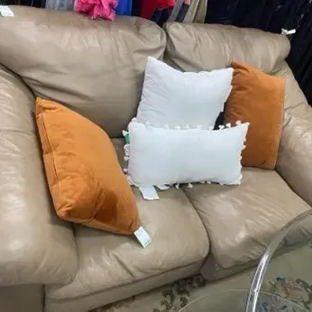 Sale Photo Thumbnail #21: Padded tan leather loveseat styled with two white and two rust-orange accent pillows.