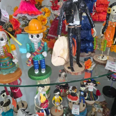 Sale Photo Thumbnail #62: Collection of vibrant Mexican Day of the Dead Catrina folk art figures and calaveras displayed on glass shelving.