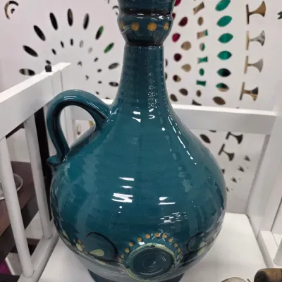 Sale Photo Thumbnail #106: Hand-painted deep teal ceramic decanter with handle, featuring yellow dotted accents and floral swirl motifs around the base.
